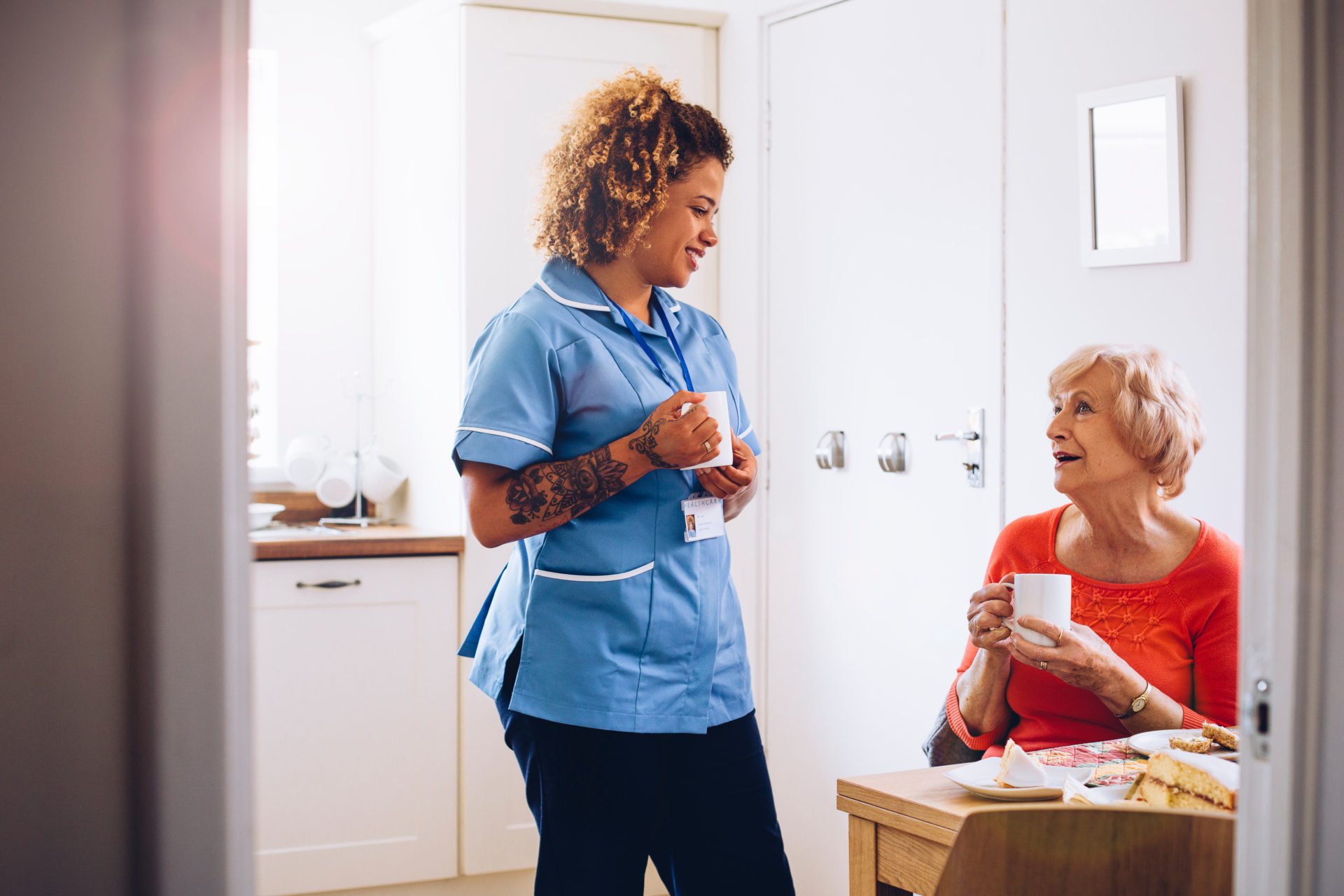 home caregiver talking to her patient in her kitchen as they drink tea and eat sponge cake.